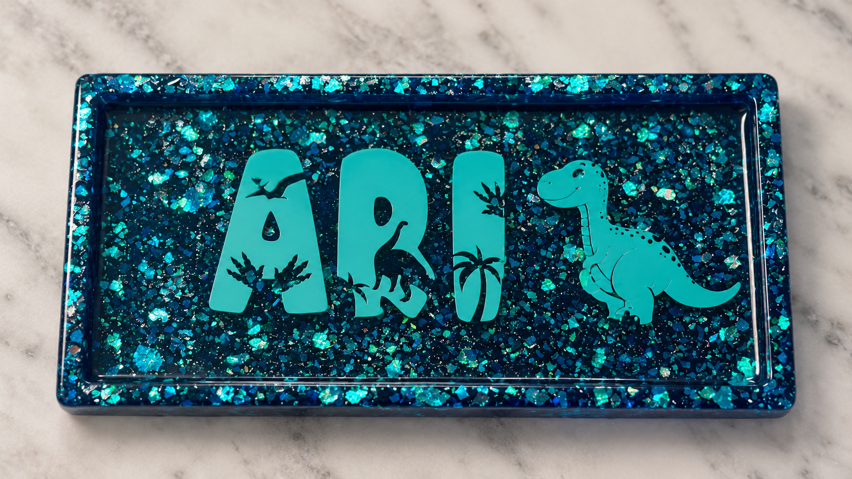 Blue glitter resin tray personalized with the name Ari and dinosaur details